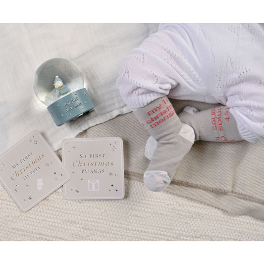 Two baby socks in grey and red with holiday text, laid on soft fabric