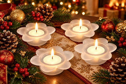 Four white flower-shaped candle holders with lit tealights, arranged on a festively decorated table.