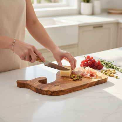 Fish-shaped wooden board with sliced cheese, prosciutto, and grapes; knife resting on top