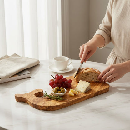 Fish-shaped wooden cutting board with bread, cheese, grapes, and a cup on table