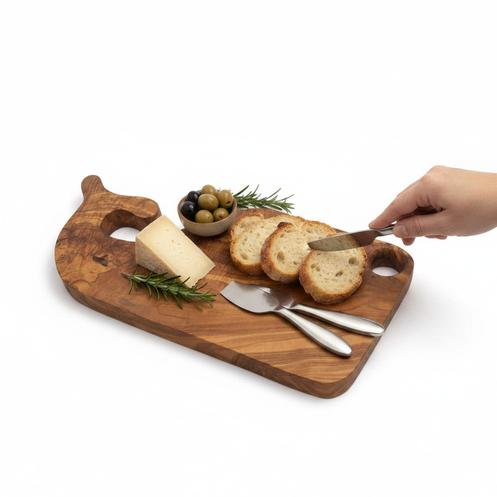 Fish-shaped wooden cutting board with bread slices, olives, rosemary, and butter knife