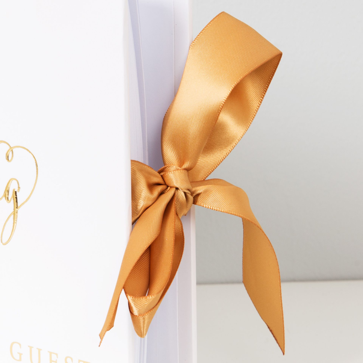 Gold satin bow ribbon tied to a white wedding guest book cover spine