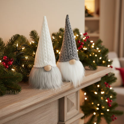Two knitted Christmas gnome decorations with tall pointed hats and fluffy beards, displayed on a wooden mantel with holiday greenery and warm string lights in the background.
