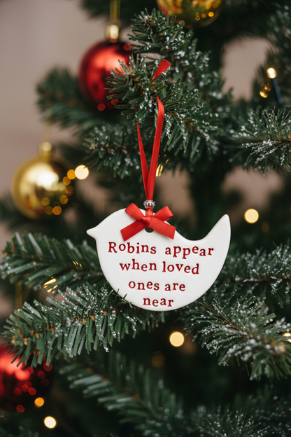 A white ceramic bird-shaped hanging ornament with red embroidered text reading 'Robins appear when loved ones are near' and a red ribbon loop at the top.