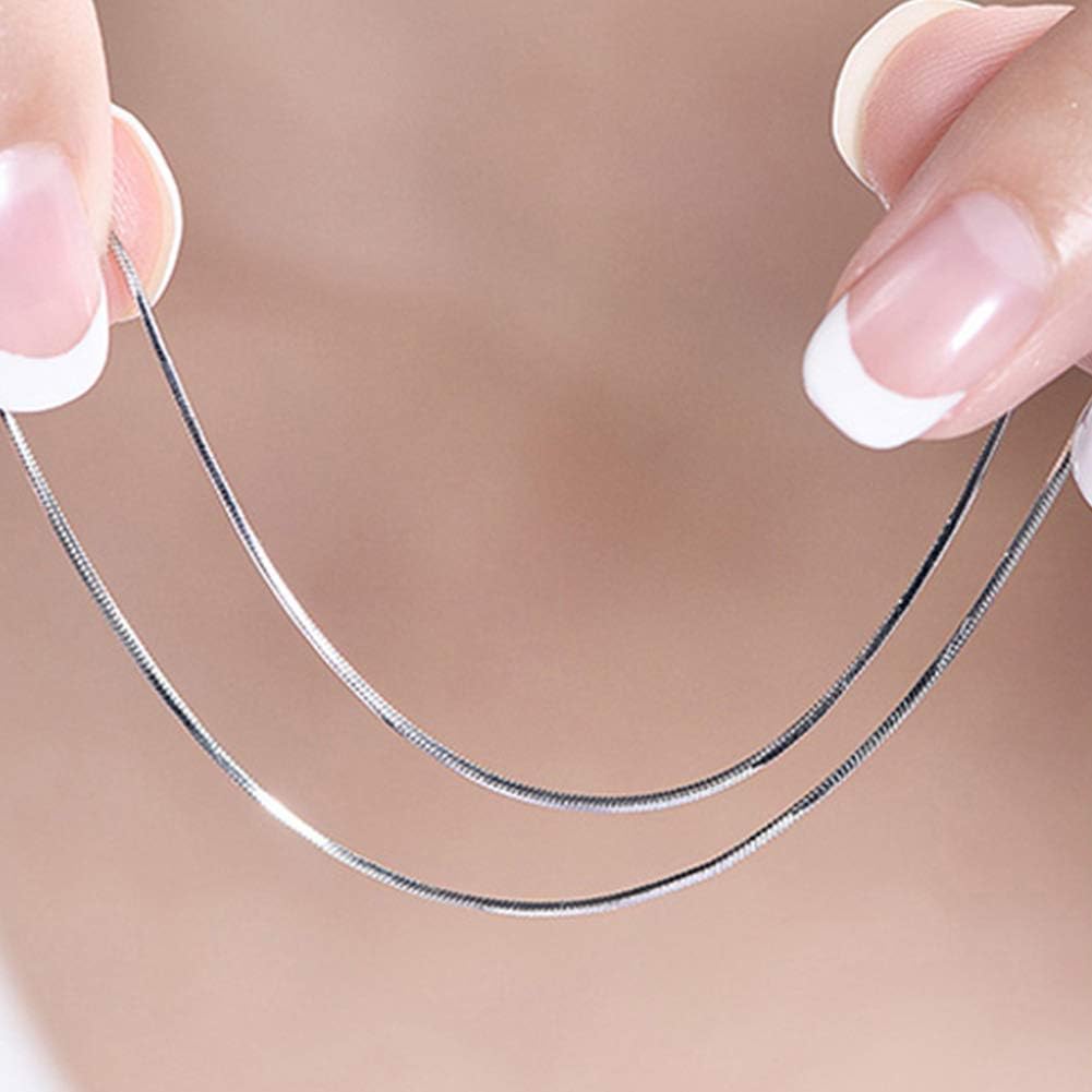A close-up of a delicate silver snake chain necklace held between two hands with French-tipped nails against a soft beige skin background.