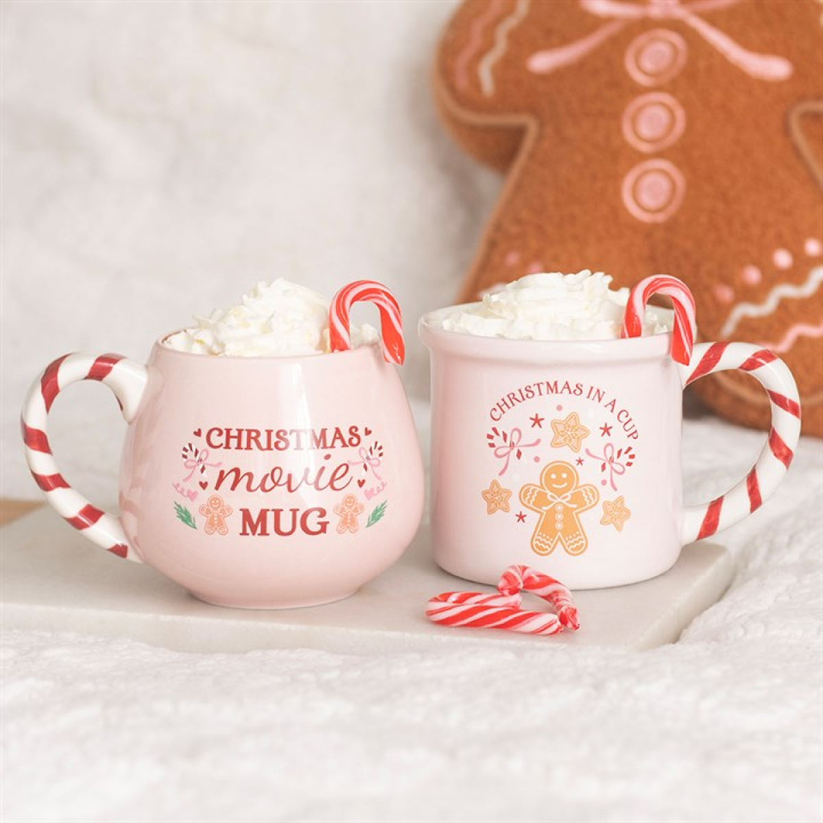 Two pink ceramic mugs with candy-cane handles; one says Christmas movie mug