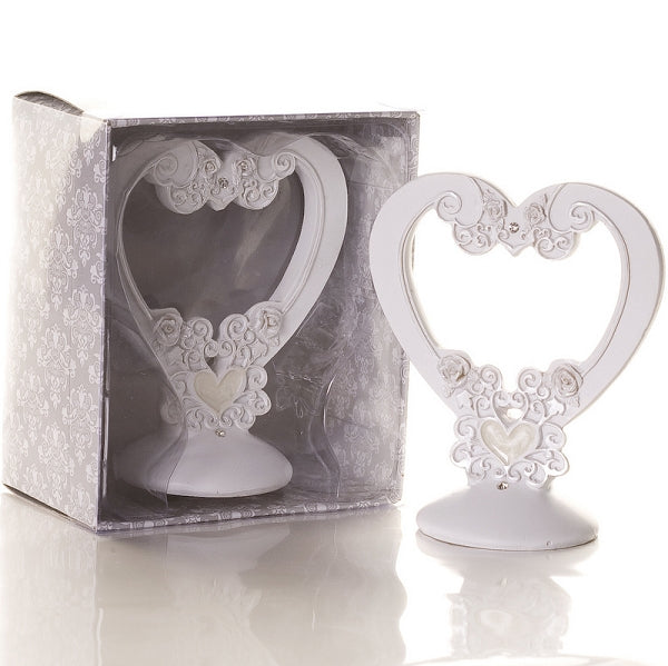A white decorative heart-shaped candle holder with ornate scrollwork and a small heart at the center, shown both standing outside its box and inside its patterned gift packaging on a white reflective surface.