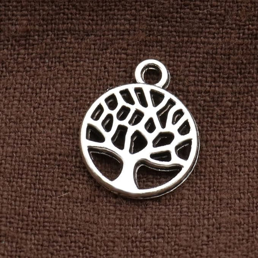 A silver tree-of-life pendant charm with a circular cutout design and top loop, shown on a textured brown fabric background.