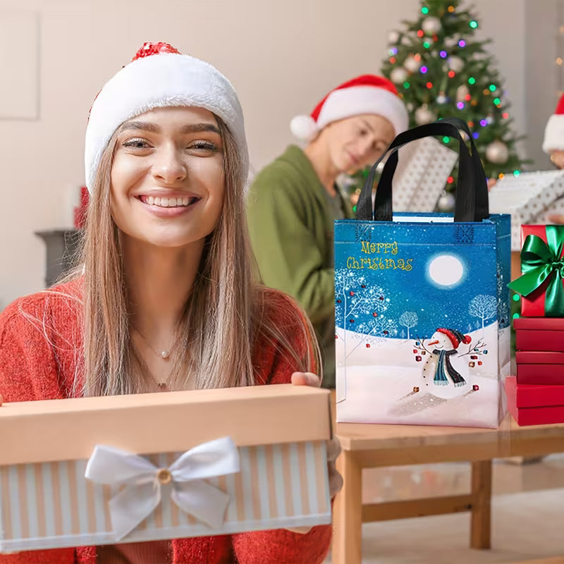 A festive Christmas gift bag with a winter scene print and 'Merry Christmas' text, held next to a wrapped gift box in a cozy holiday setting with people in Santa hats in the background.