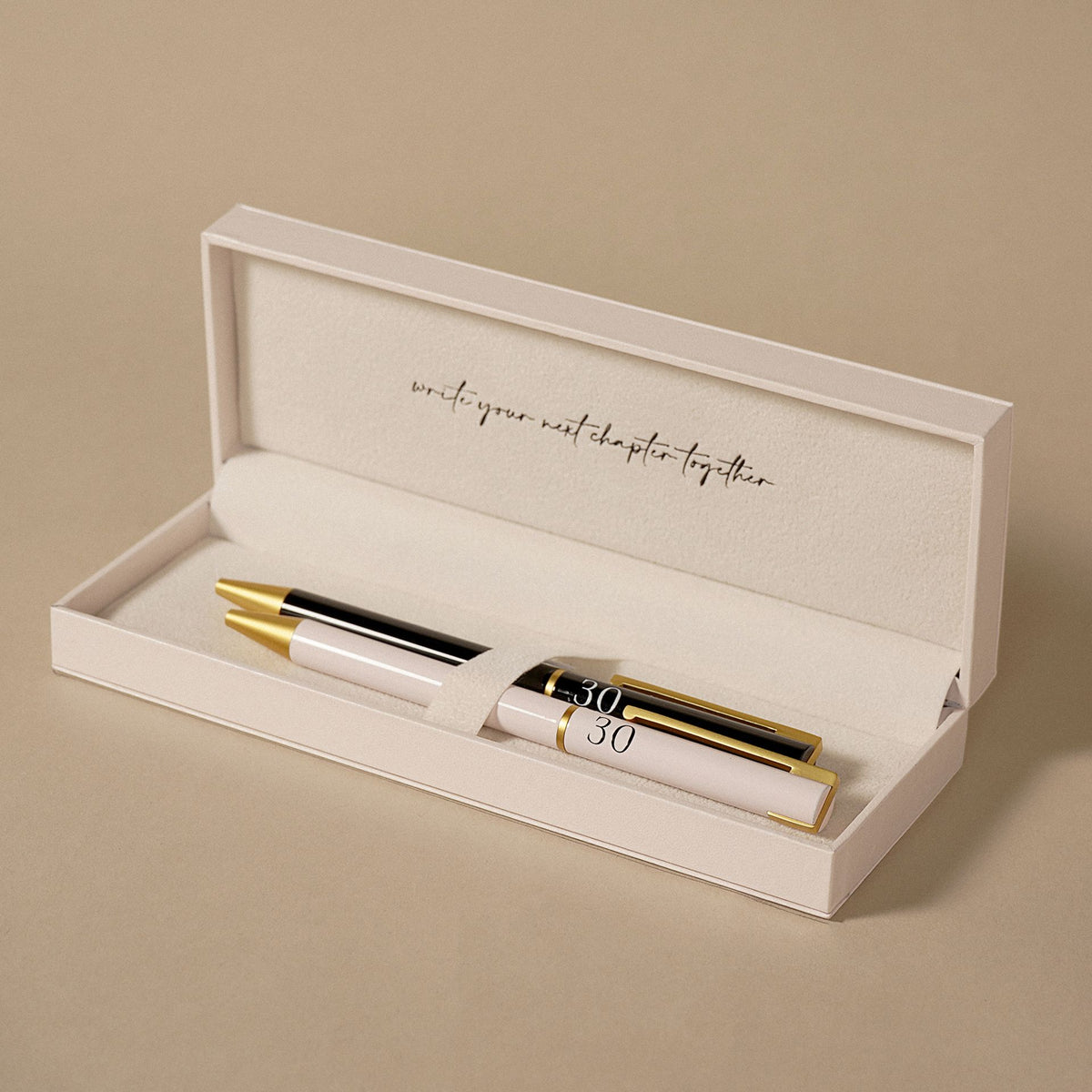 Open gift box holding two pens, black and blush with gold caps