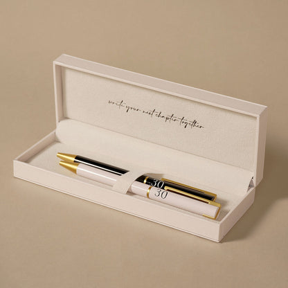 Open gift box holding two pens, black and blush with gold caps