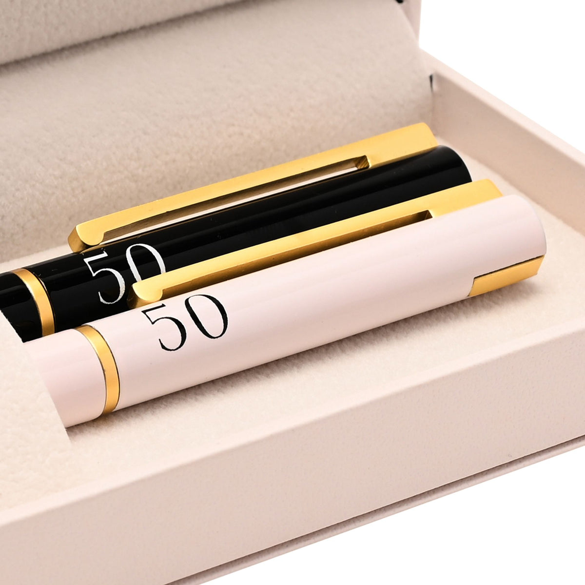 Pair of anniversary pens with gold ends: black pen marked 50 and pale pink pen