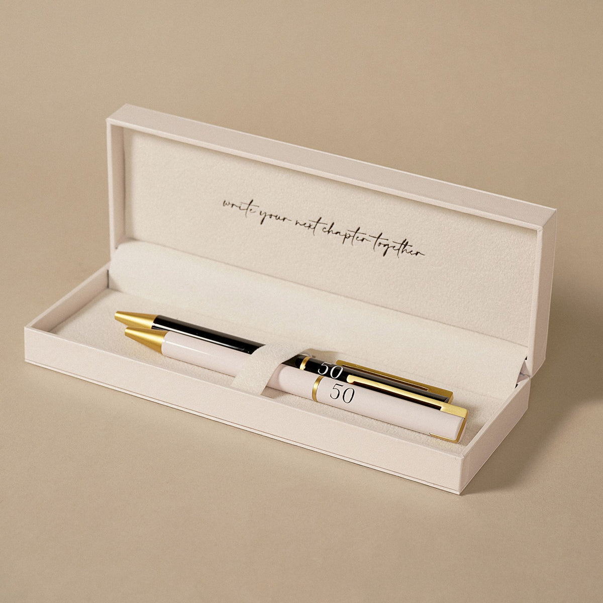 Open gift box holding two anniversary pens, black and pale pink with gold accents