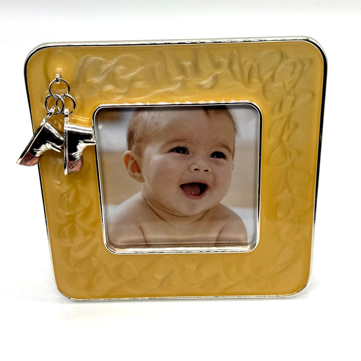 A square yellow picture frame with an embossed floral border and a silver-tone hanging initial 'A' charm, shown with a baby photo insert on a white background.