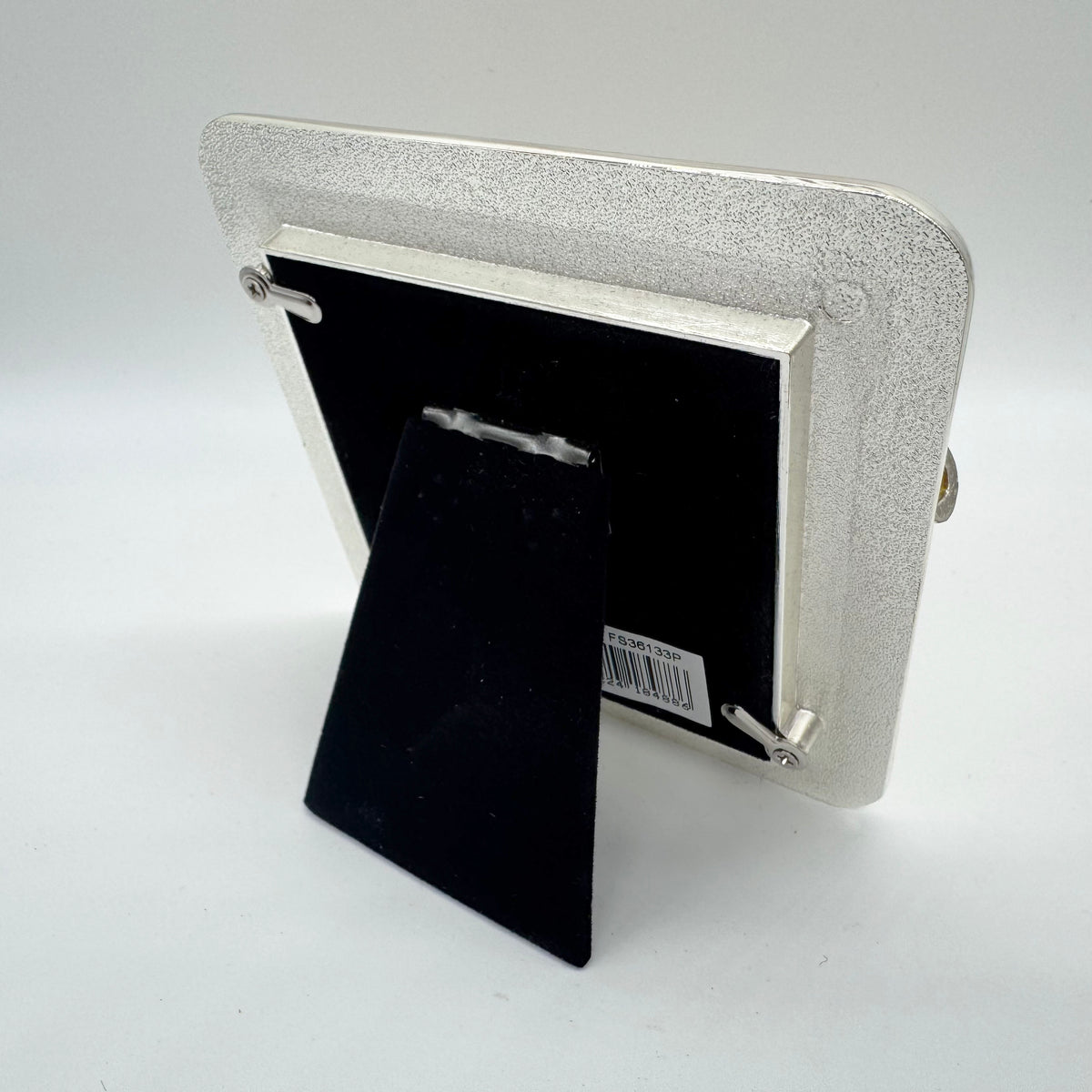 A silver picture frame with a textured finish, shown from the back with its black velvet insert and built-in display stand.