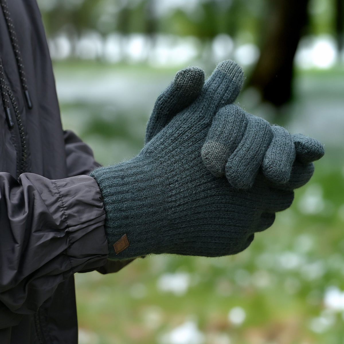 Green rib-knit gloves with leather logo patch, worn over jacket cuff