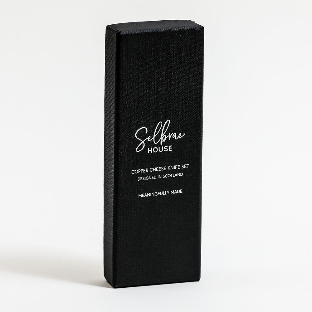 Black box packaging for copper cheese knife set with white brand text