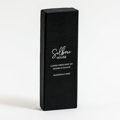 Black box packaging for copper cheese knife set with white brand text