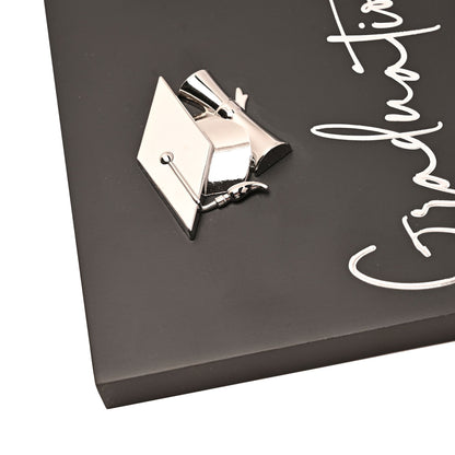 Silver graduation cap emblem on black photo frame, with white chalk-style doodles