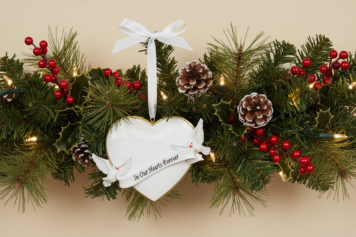 Heart-shaped ornament with two doves and 'In Our Hearts Forever' banner hanging on a festive garland