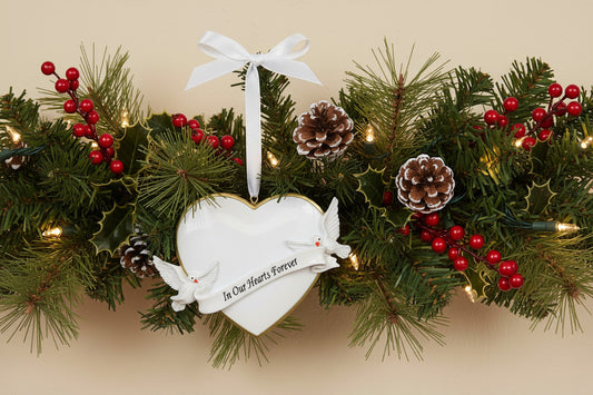 Heart-shaped ornament with two doves and 'In Our Hearts Forever' banner hanging on a festive garland
