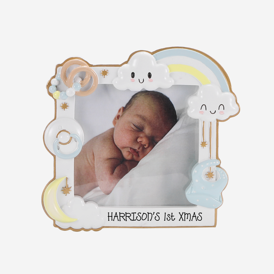 A personalized baby photo frame with a whimsical cloud, rainbow, and moon design. The frame is shown holding a photo of a sleeping newborn baby, with the text 'HARRISON'S 1st XMAS' written at the bottom.