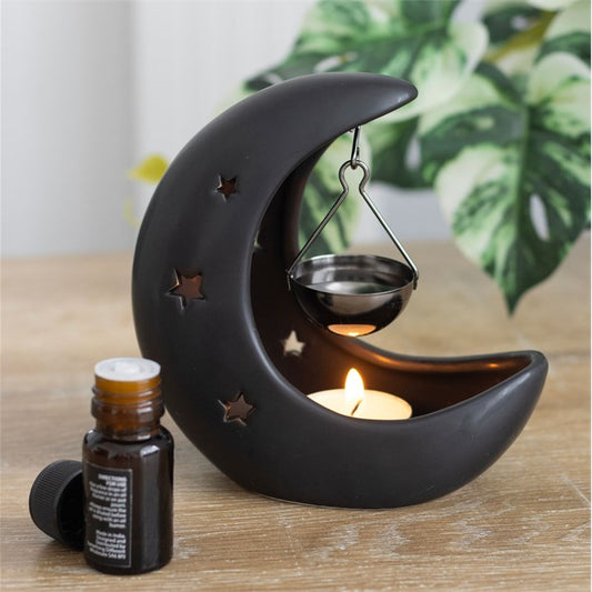 Black crescent moon oil burner with hanging ladle, lit tealight, and oil bottle