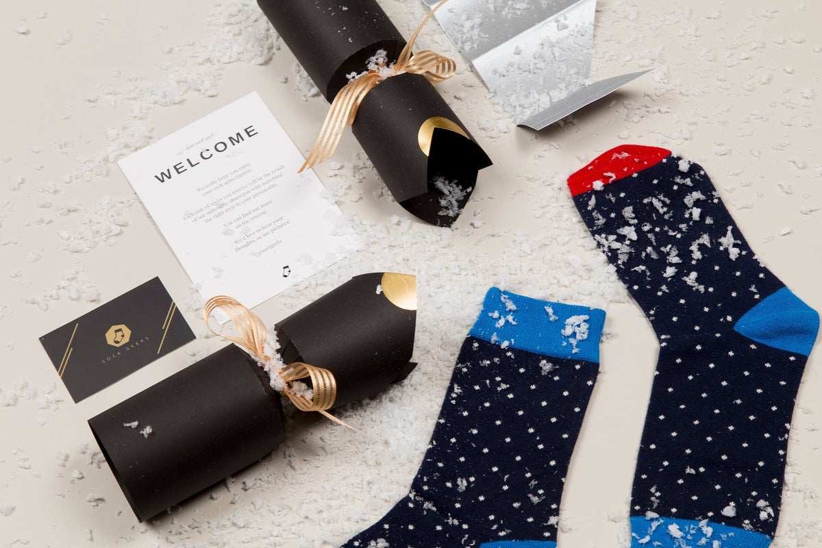 Two pairs of patterned socks on a textured surface with gift wrappings and a card.