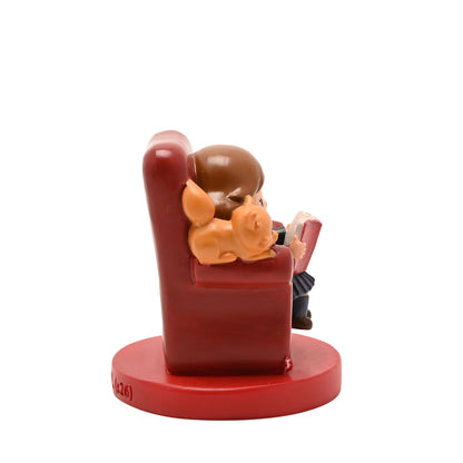 Side view of red armchair figurine: girl reading a red book with orange pet