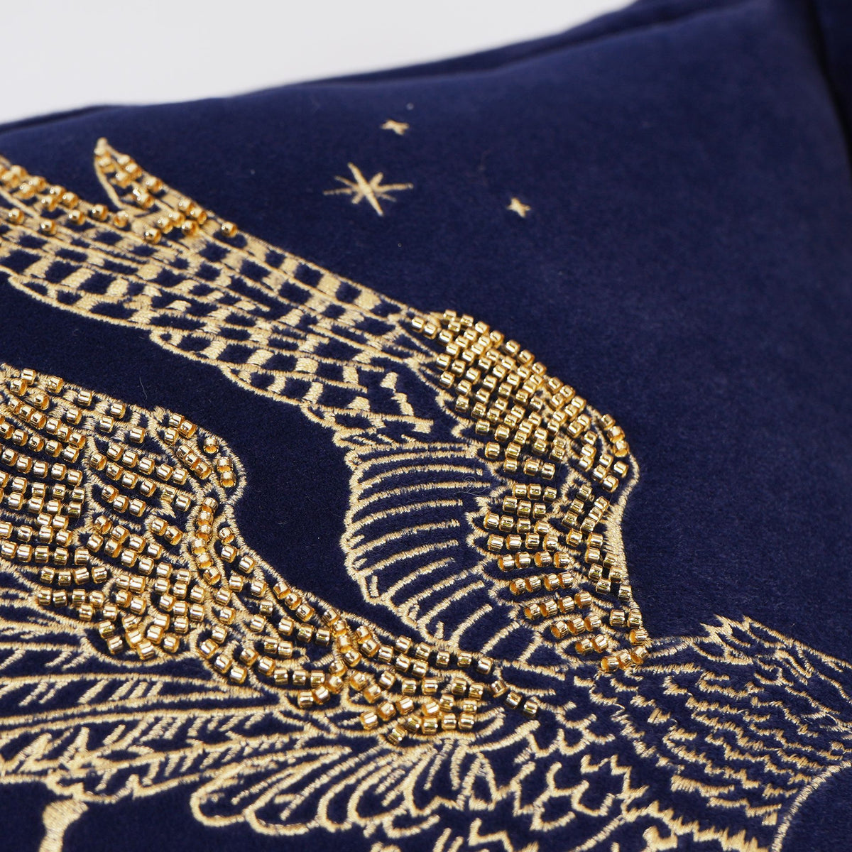 Close-up of gold-stitched Buckbeak wings on navy velvet cushion