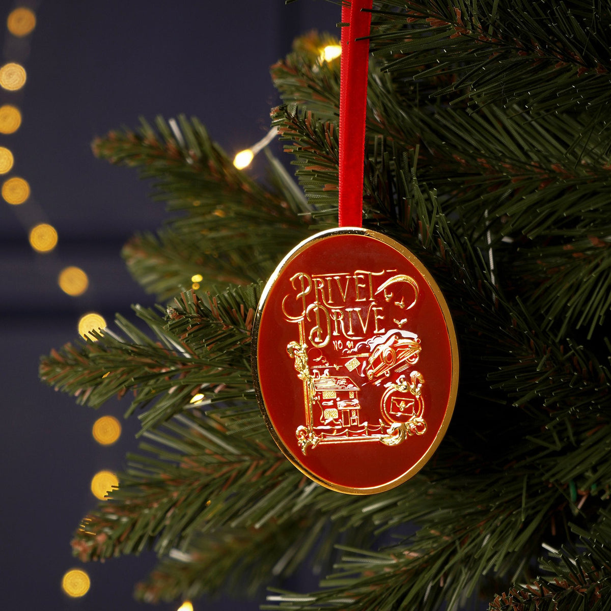 Red oval ornament with gold Privet Drive design and red hanging ribbon on a tree