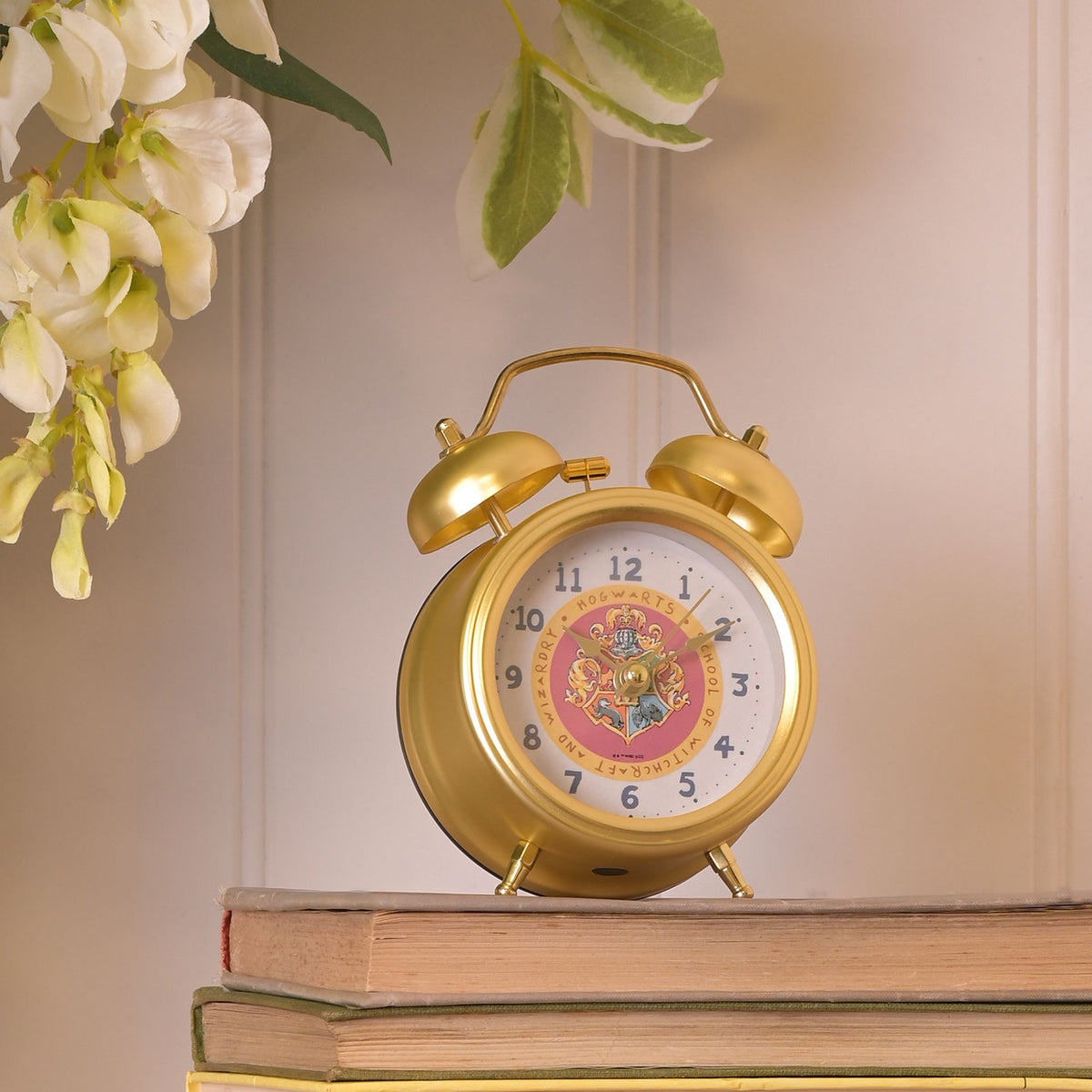 Gold twin-bell alarm clock on tabletop with Hogwarts crest face