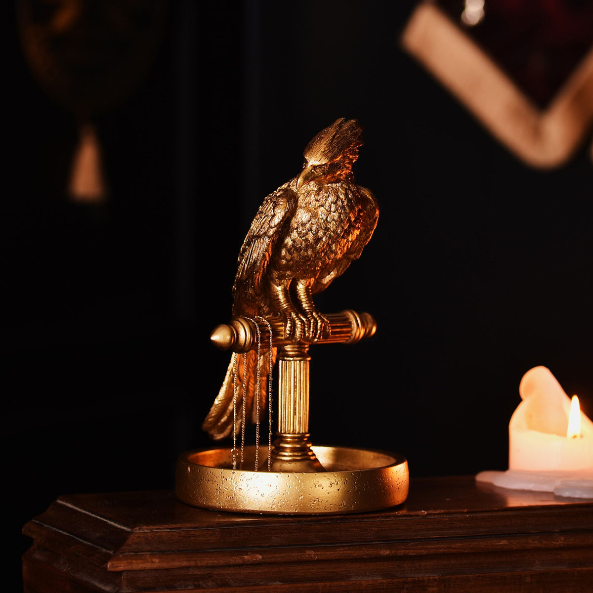 Bronze-tone Fawkes bird jewellery stand with round tray beside a lit candle