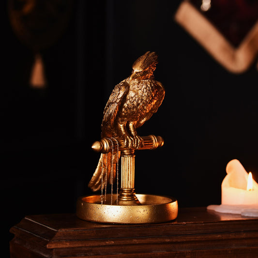 Bronze-tone Fawkes bird jewellery stand with round tray beside a lit candle