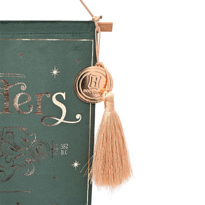 Ollivanders banner detail: round H seal charm with beige tassel fringe on dark green cloth