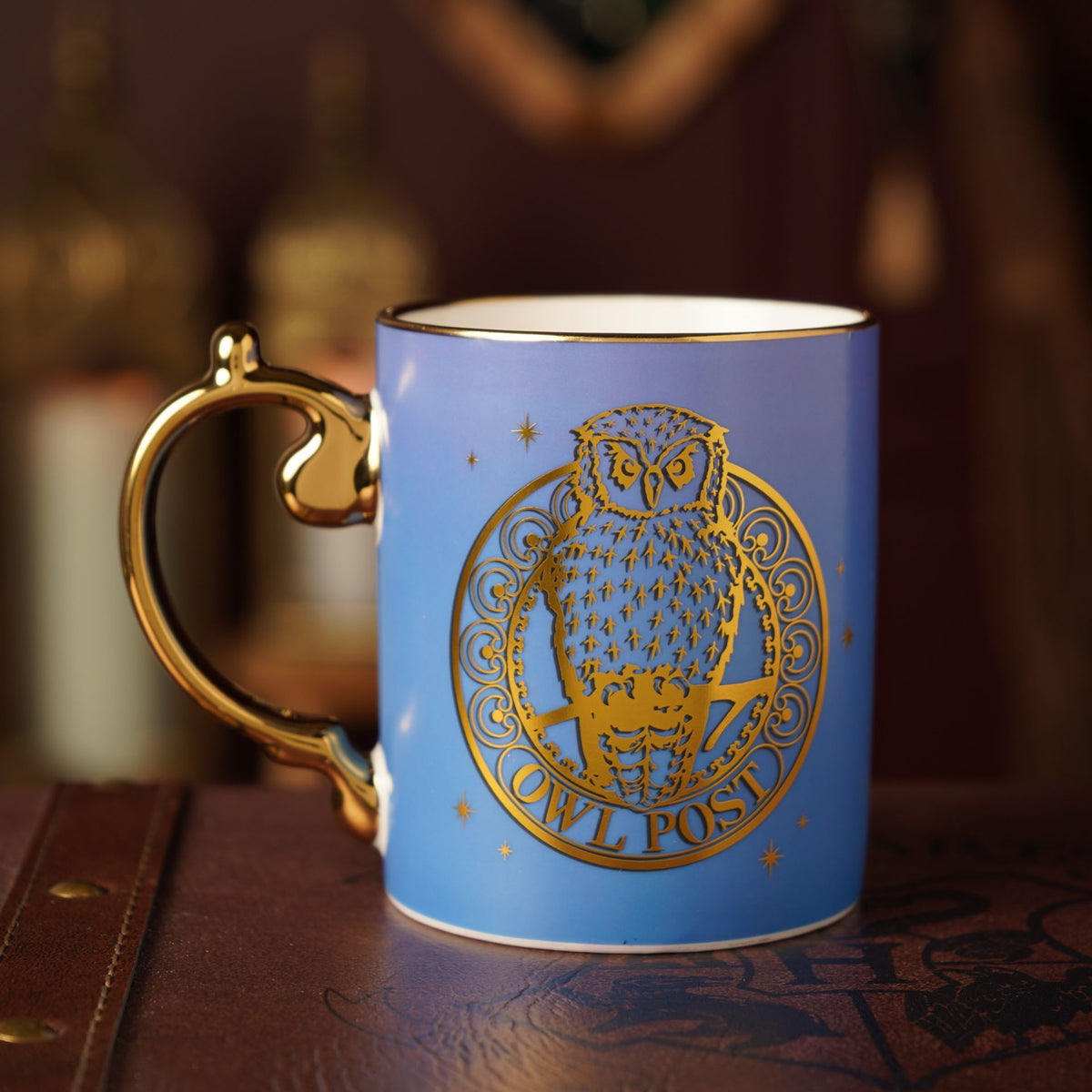 Blue ceramic mug with gold owl emblem and Owl Post text, gold handle.