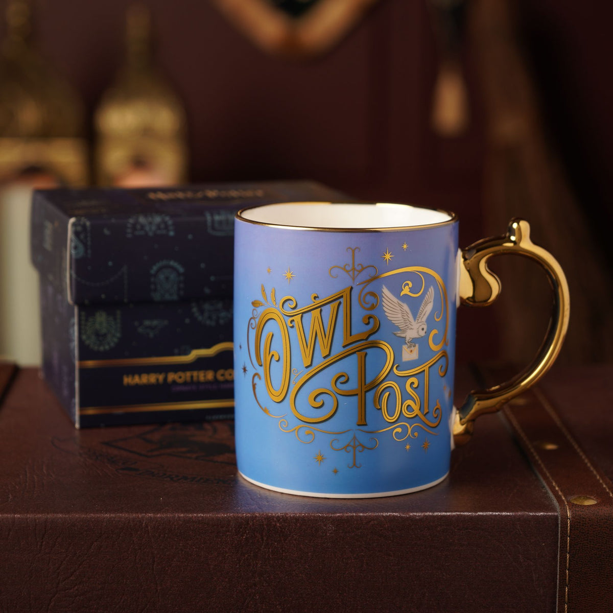 Blue Owl Post mug with gold handle, with dark gift box behind.