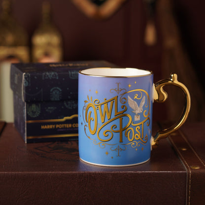 Blue Owl Post mug with gold handle, with dark gift box behind.