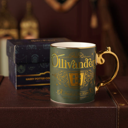 Dark green collectible mug with gold “Ollivanders” design, gold handle, and box