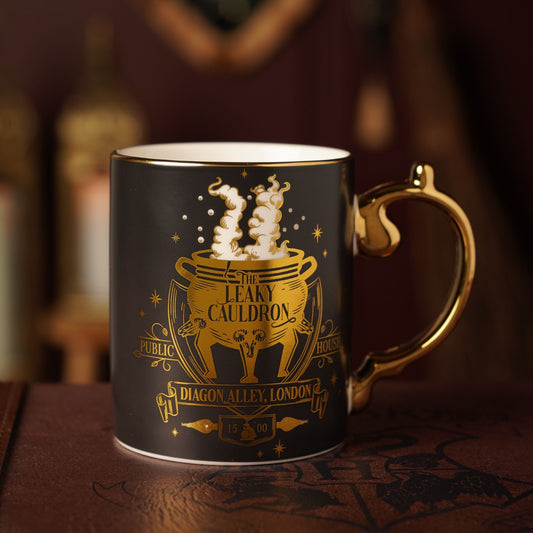 Dark mug with gold Leaky Cauldron crest and star accents; curved gold handle