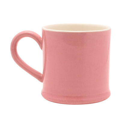 Pink ceramic mug with curved handle, smooth glaze, and partial character design, side view