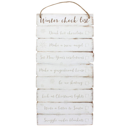 A rustic vertical wooden hanging sign with a jute rope loop at the top, featuring a white distressed finish and the words 'Winter check list' followed by holiday-themed checklist items in gray script with checkboxes.