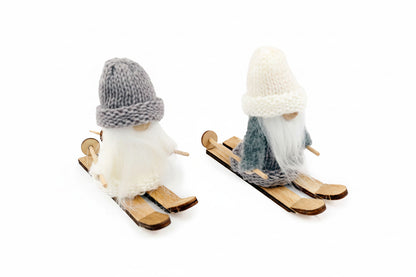Two small gnome figurines dressed as skiers on a white background. One gnome wears a gray knit hat and beard with a blue-gray outfit, and the other wears a cream knit hat and beard with a blue-gray outfit.