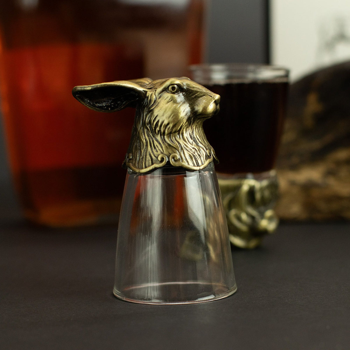 Clear shot glass with antique bronze fox-like creature topper, close-up