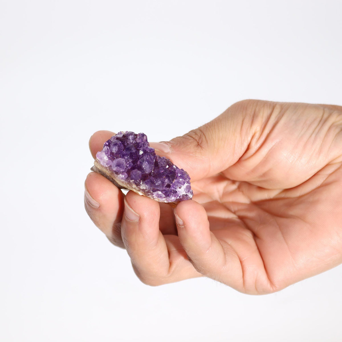 Natural amethyst cluster held in hand, purple crystals on tan rock base