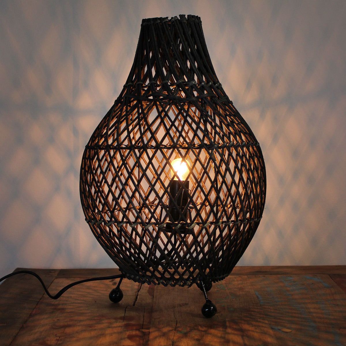 Dark rattan table lamp with glowing bulb behind teardrop lattice shade