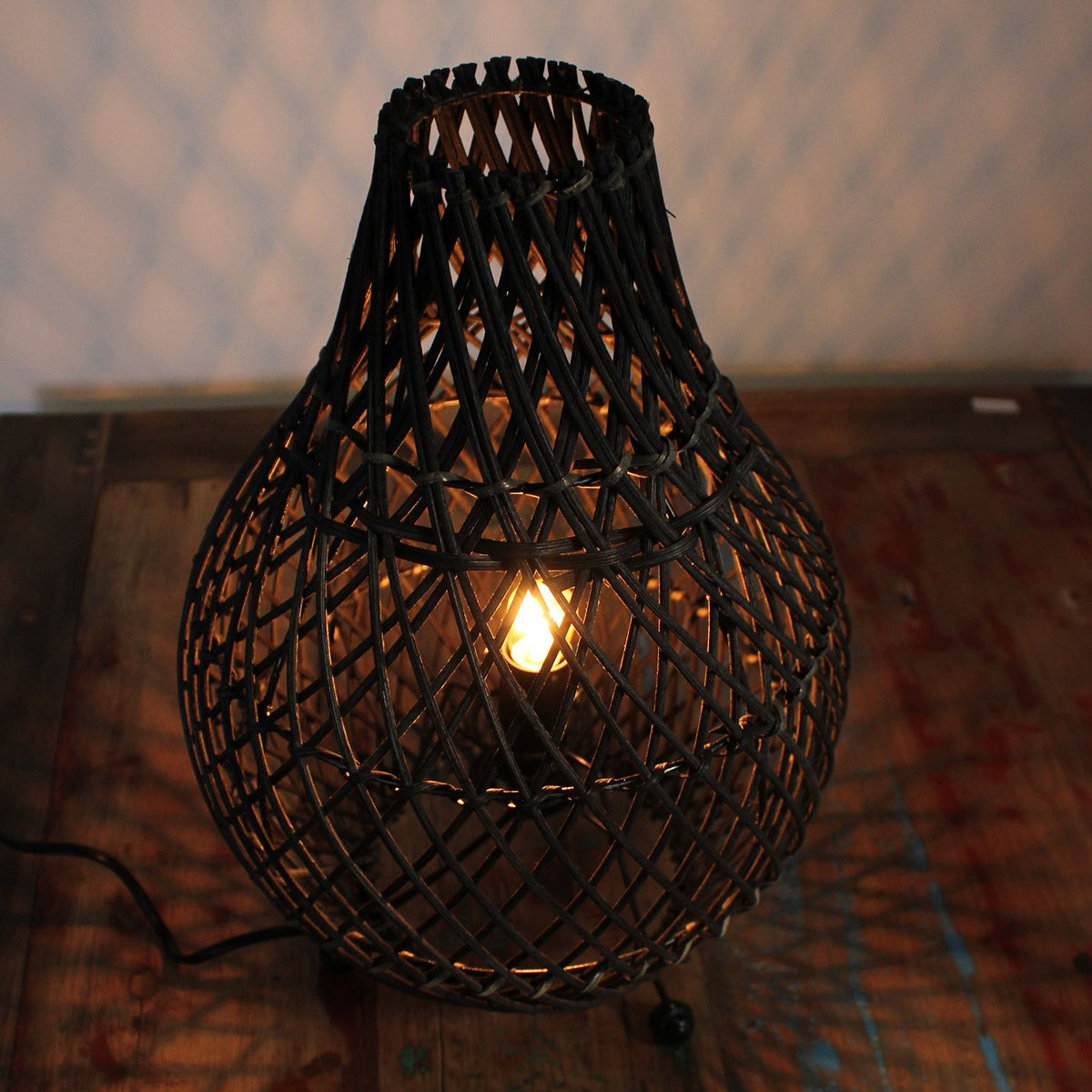 Lit black rattan teardrop table lamp with warm light inside lattice shade