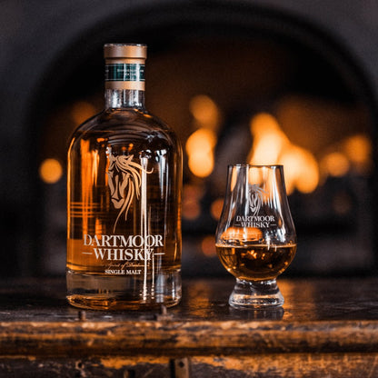 Amber single malt whisky bottle with matching branded glass on a wooden surface.