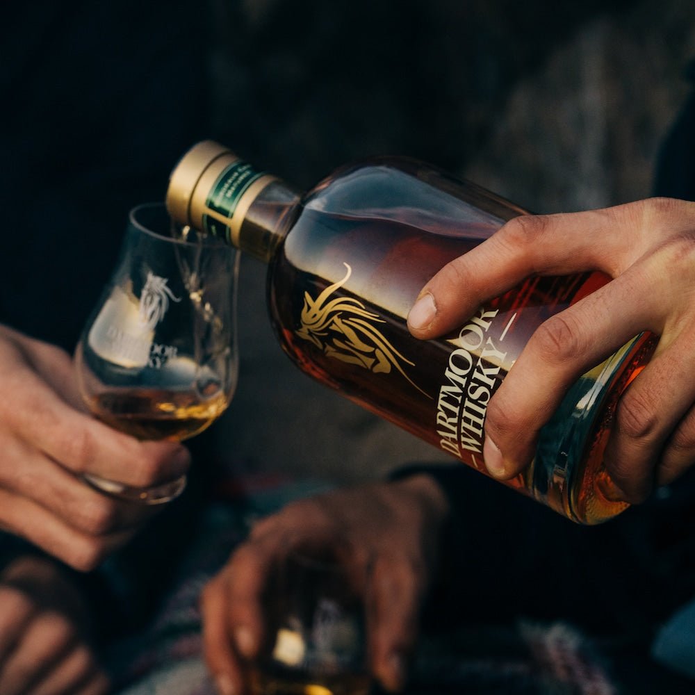 Dartmoor Whisky bottle tilted as it pours, amber liquid and label visible.