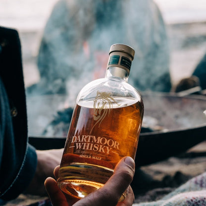 Dartmoor Whisky bottle held in hand, amber liquid visible through clear glass.